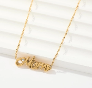 Detalle del collar dorado Mom con circonita incrustada sobre fondo blanco texturizado