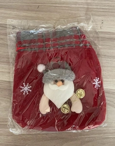 Detail of red fabric Christmas gift bag with plush Santa Claus and golden bells