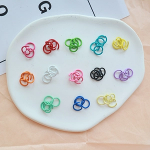 Assorted colorful paint-coated metal jump rings for DIY jewelry making on a ceramic tray