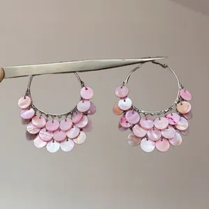 Détail de créoles argentées avec pendentifs en nacre rose tenues par une pince