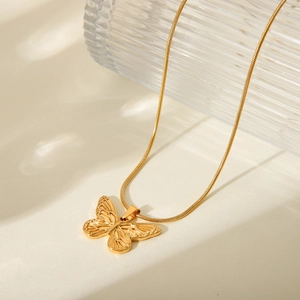 Detail of 18K gold butterfly pendant with elegant snake chain on a soft beige background