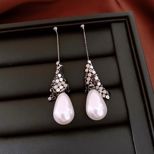 Detailed close-up of pear-shaped pearl earrings with silver chain and scale texture