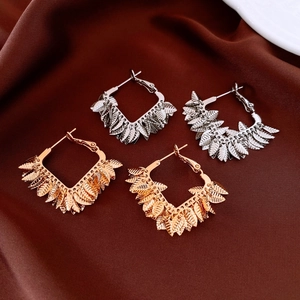 Detail of gold and silver plated leaf charm hoop earrings on elegant silk fabric