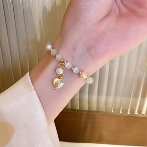 Vue rapprochée d'un bracelet de perles oeil-de-chat blanc et pendentif coeur au poignet