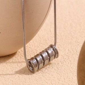 Silver cylinder spring pendant necklace on textured ceramic vase in modern minimalist style