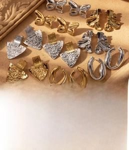 Detailed close-up of titanium steel butterfly and triangular earrings in gold and silver finish
