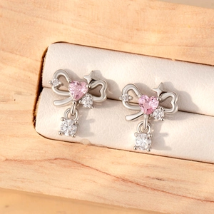 Silver bow earrings with pink heart gemstones on a white jewelry box cushion
