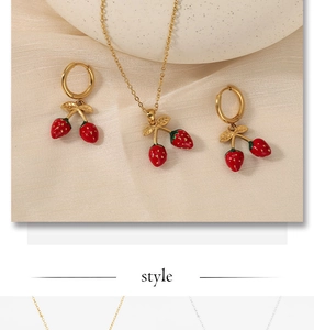 Détail d'une parure de bijoux fraise en émail rouge avec chaîne dorée et boucles