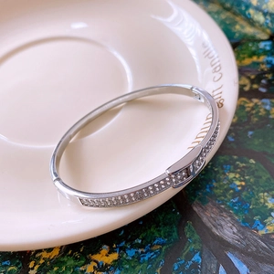Close-up of silver-tone zircon pavé bangle with H-shaped clasp on decorative plate