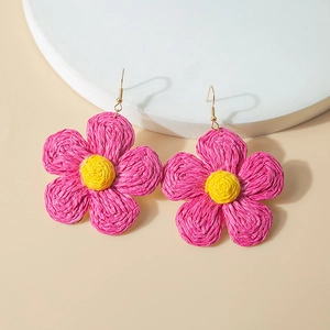Detail of handmade woven raffia flower earrings with yellow and pink petals and gold hooks