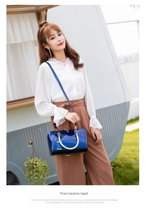 Detail of navy blue patent leather handbag with gold hardware shown in a lifestyle street setting