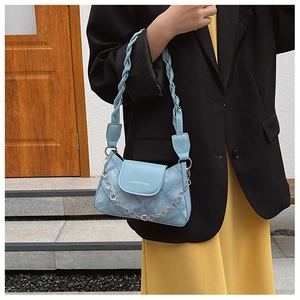 Detail of light blue denim texture bag with floral chain and woven handle on model