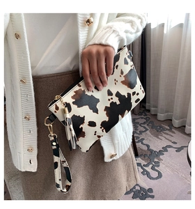 Detail of cow print envelope clutch with leather tassel and wristlet strap held by hand