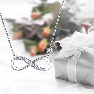 Close-up of infinity pendant necklace with pavé diamonds next to a ribbon gift box