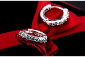 Macro shot of silver S925 huggie earrings with row diamonds on red silk ribbon