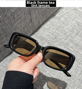 Detail of square sunglasses featuring black frame and tea lenses held against fabric