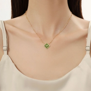 Detail of green clover pendant necklace on gold chain worn by a fashion model