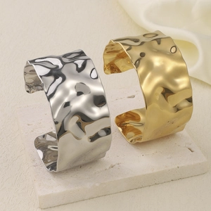 Detail view of gold and silver wavy wide cuff bracelets on white stone and satin