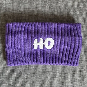 Detail of purple knitted sports headband featuring white HO letter patch and ribbed texture
