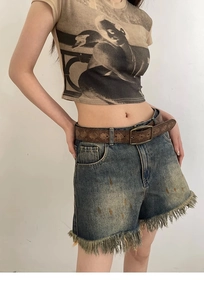 Detail of vintage embossed brown leather belt with bronze buckle on denim shorts