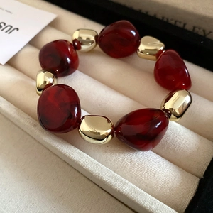 Close-up of deep red resin beads and polished gold metal beads on a beige velvet tray