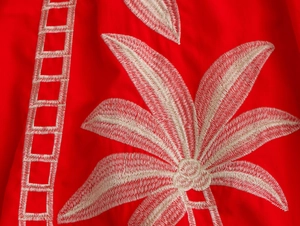 Nahaufnahme des roten Urlaubsstoffs mit weißen Palmblatt- und geometrischen Stickereien