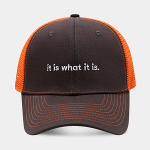 Detail of white embroidery 'it is what it is.' on a mesh trucker baseball cap