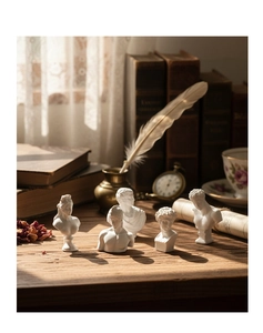 Artistic close-up of four mini Greek resin busts on a vintage desk with quills