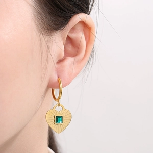 Close-up of heart-shaped gold earring featuring a square green gemstone on the ear