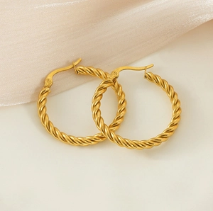Détail macro de boucles d'oreilles créoles torsadées en acier doré sur fond de soie