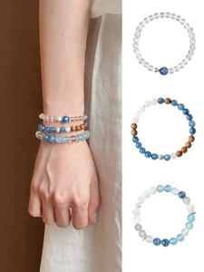 Detailansicht von Armbändern aus Bergkristall und Cyanit am Handgelenk und weißem Hintergrund.