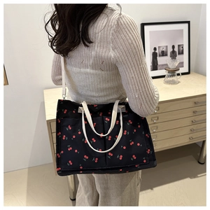 Detail of a black canvas tote bag with red cherry prints and white shoulder strap