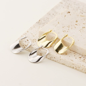 Close-up of irregular U-shaped gold and silver earrings on a beige stone surface