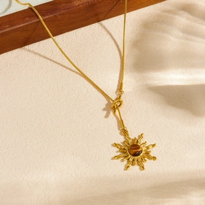 Gold sun pendant necklace with tiger eye stone and snake chain under natural shadows