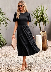 Close-up of a black smocked midi dress with tiered skirt in a tropical garden setting