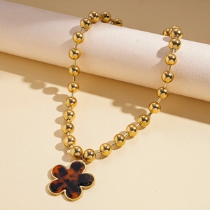 Close-up of golden beaded chain necklace featuring a vintage tortoiseshell flower pendant