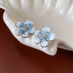 Macro view of blue gradient crystal flower earrings with rhinestone centers on shell