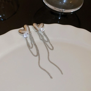 Detailed view of silver heart earrings with rhinestone tassels on a white porcelain dish