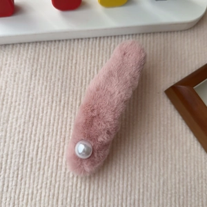 Detail einer rosa Plüsch-Haarklammer mit weißer Perle auf strukturiertem Stoff