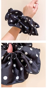 Detailed close-up of elegant black fabric scrunchie with white polka dot pattern