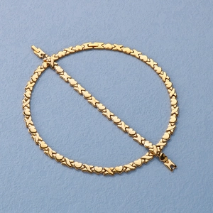 Close-up of gold heart and X symbol link necklace on a textured light blue surface