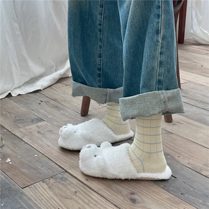 Close-up of fluffy white bunny slippers worn with striped socks and rolled-up jeans
