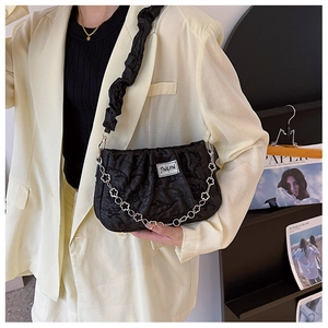 Detail of black pleated shoulder bag with decorative metallic flower chain worn by model