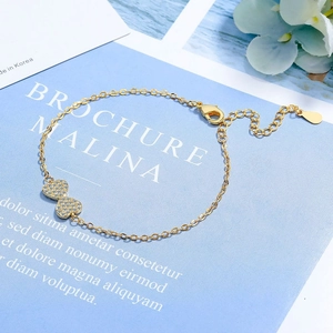 Detail of gold chain bracelet with double heart charms and zircon crystals on blue background