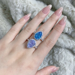 Detailed view of pear-shaped halo rings in blue and purple on a soft grey fabric background