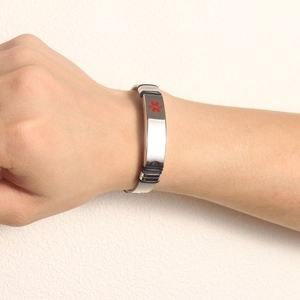 Detail of medical alert mesh bracelet in silver steel with red emergency cross symbol