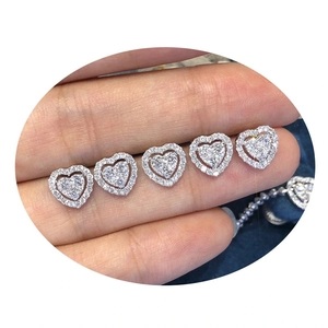 Macro shot of heart-shaped silver earrings with sparkling white gemstones on a finger