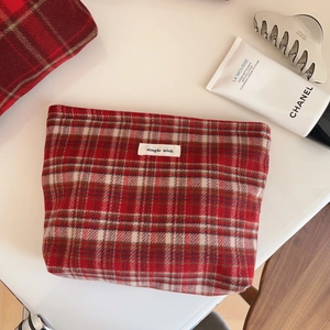 Détail de la trousse à maquillage en laine à carreaux rouges avec étiquette sur blanc