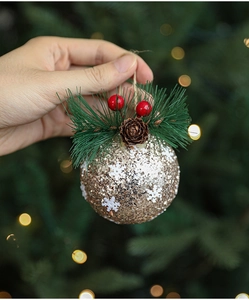 Detail of golden Christmas ball with white snowflakes, pine needles, and pine cones