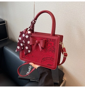Close-up of red wedding handbag with floral embroidery, bow, and silk scarf detail